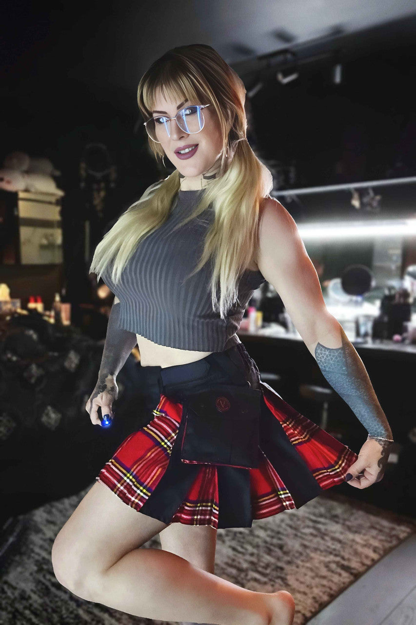 Woman in a black crop top and black and red plaid mini kilt posing in a bar setting.