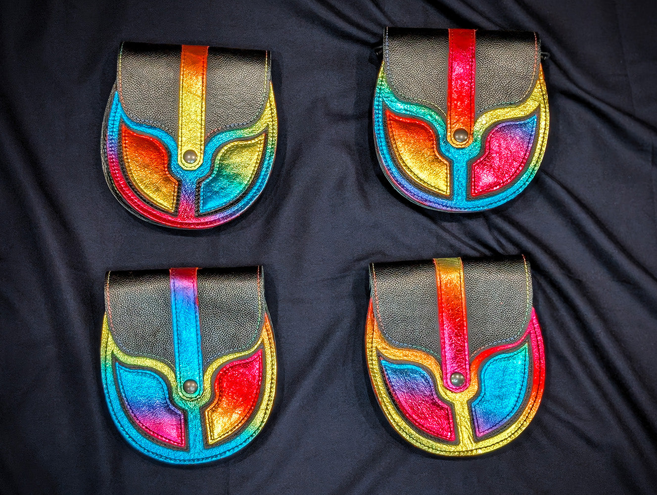 Four black leather pouches with metallic rainbow accents on a black background
