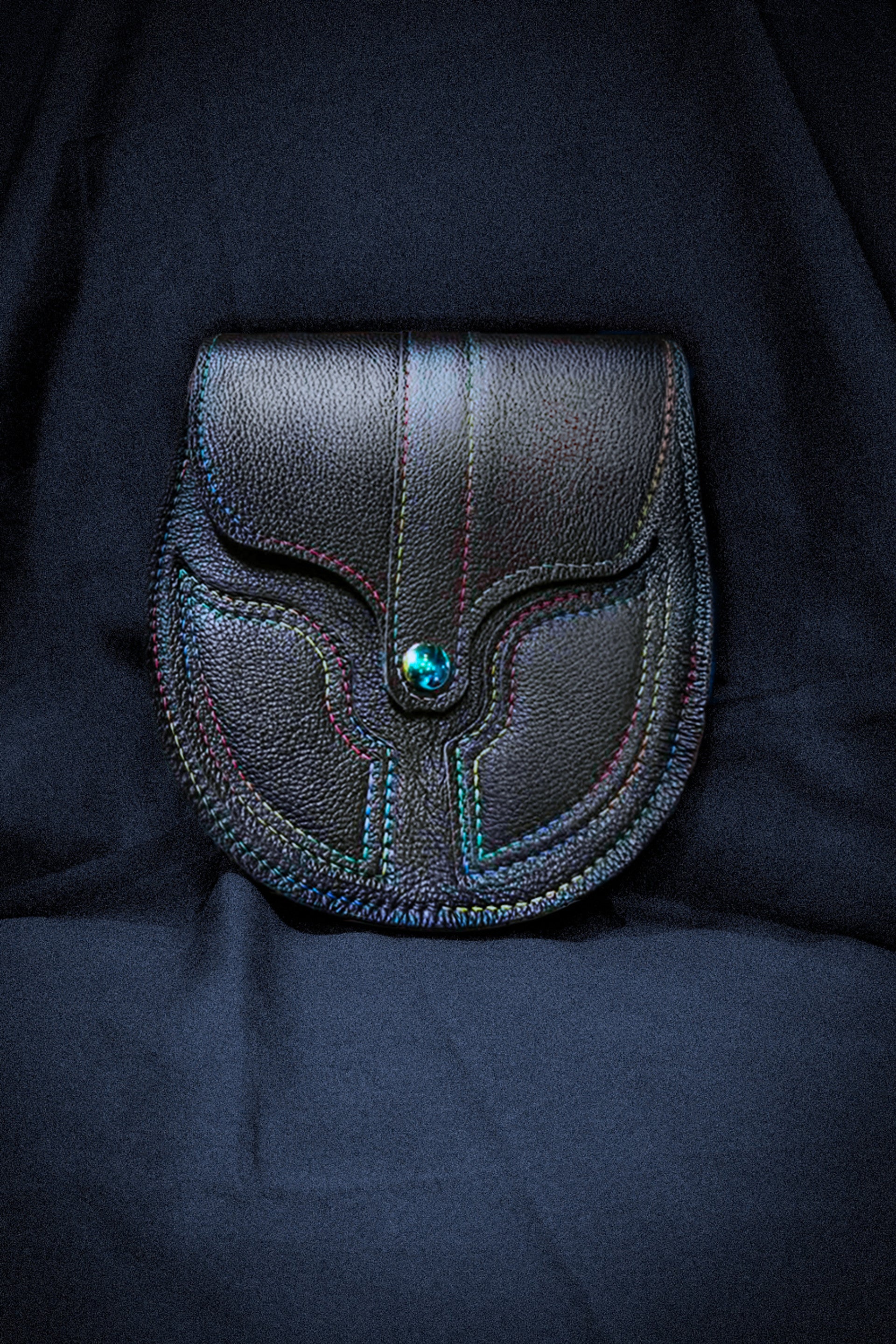Black leather sporran with rainbow sticching on a dark blue cloth background.