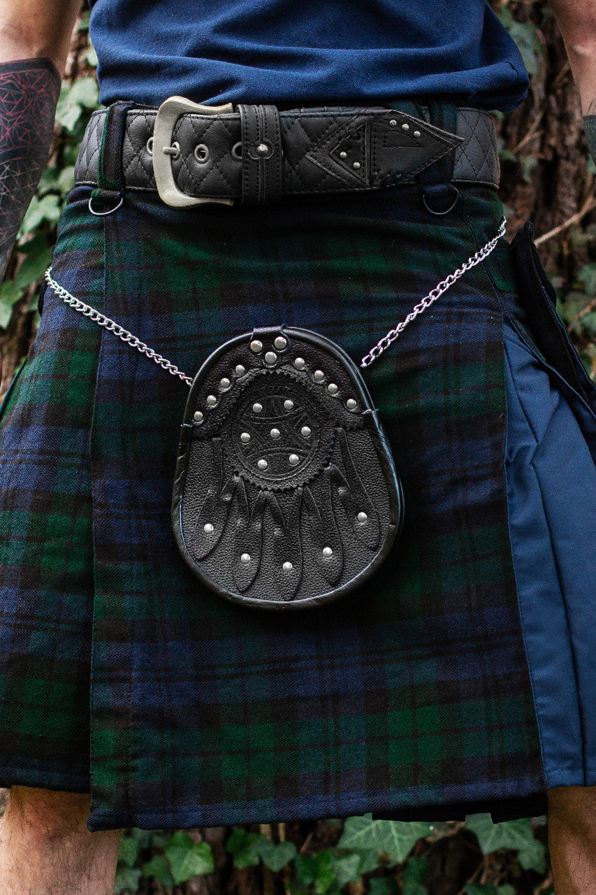 Close up of a black leather sporran with leather detailing and silver studs hanging at the front of a plaid kilt.