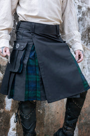 Person wearing a black kilt with green plaid pattern against a stone wall.