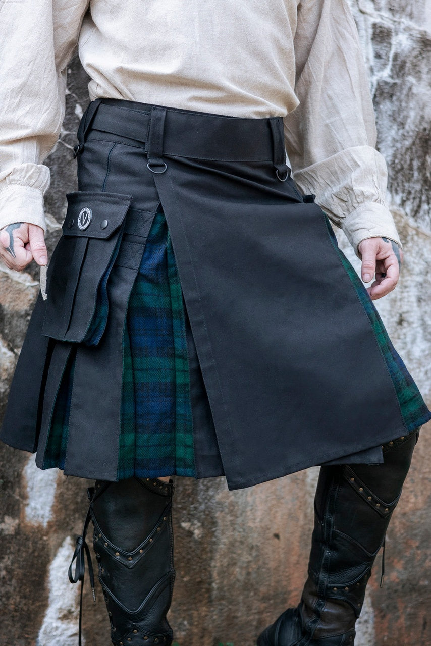 Person wearing a black kilt with green plaid pattern against a stone wall.
