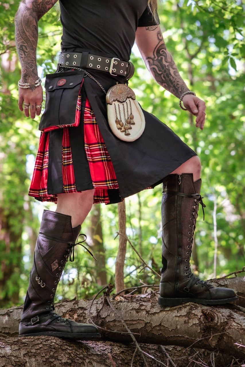 Person wearing a red and black plaid kilt with leather boots in a forest setting