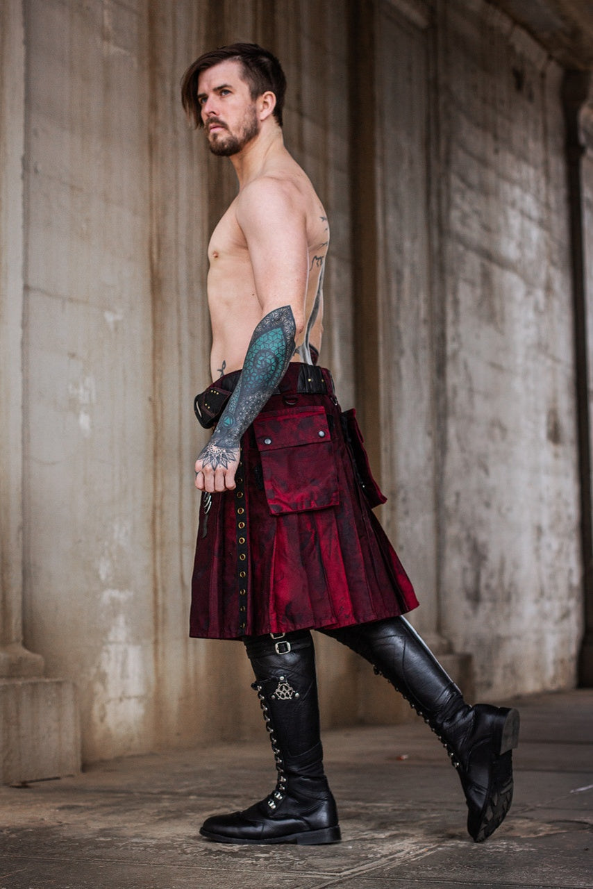 Man wearing a burgundy and black kilt and black leather boots in an industrial setting