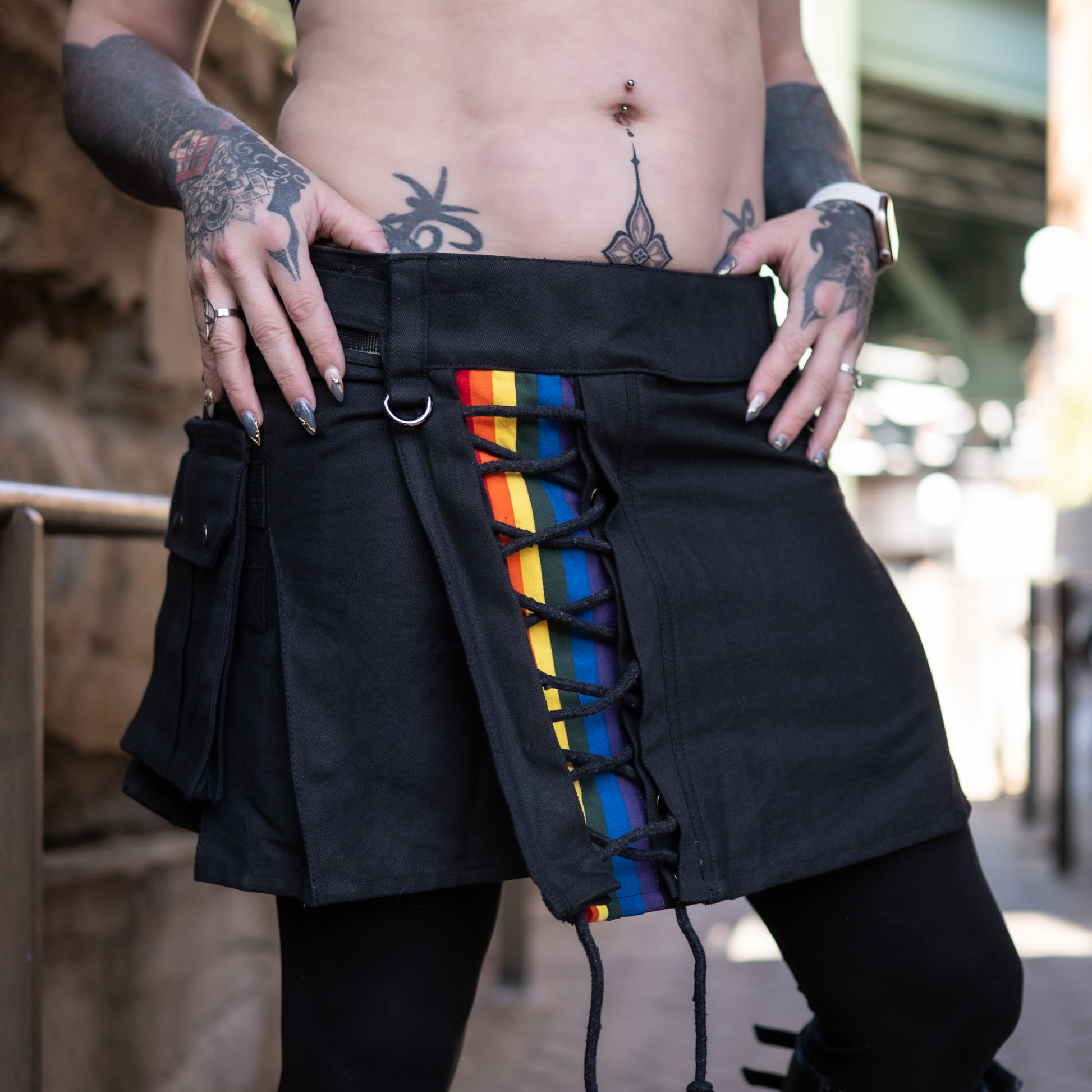Black mini kilt featuring a cross-laced section in the front panel featuring a rainbow stripe.