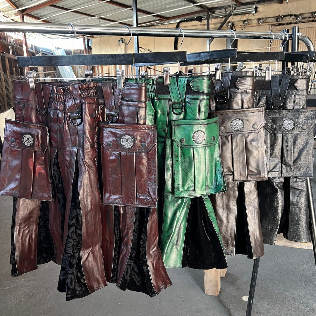 Collection of brown, green, grey, and black leather kilts on hangers in a storage area.