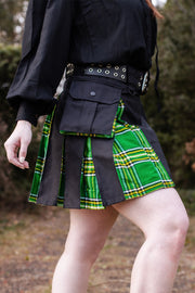 Person wearing a black outfit with a black and green plaid mini kilt in an outdoor setting