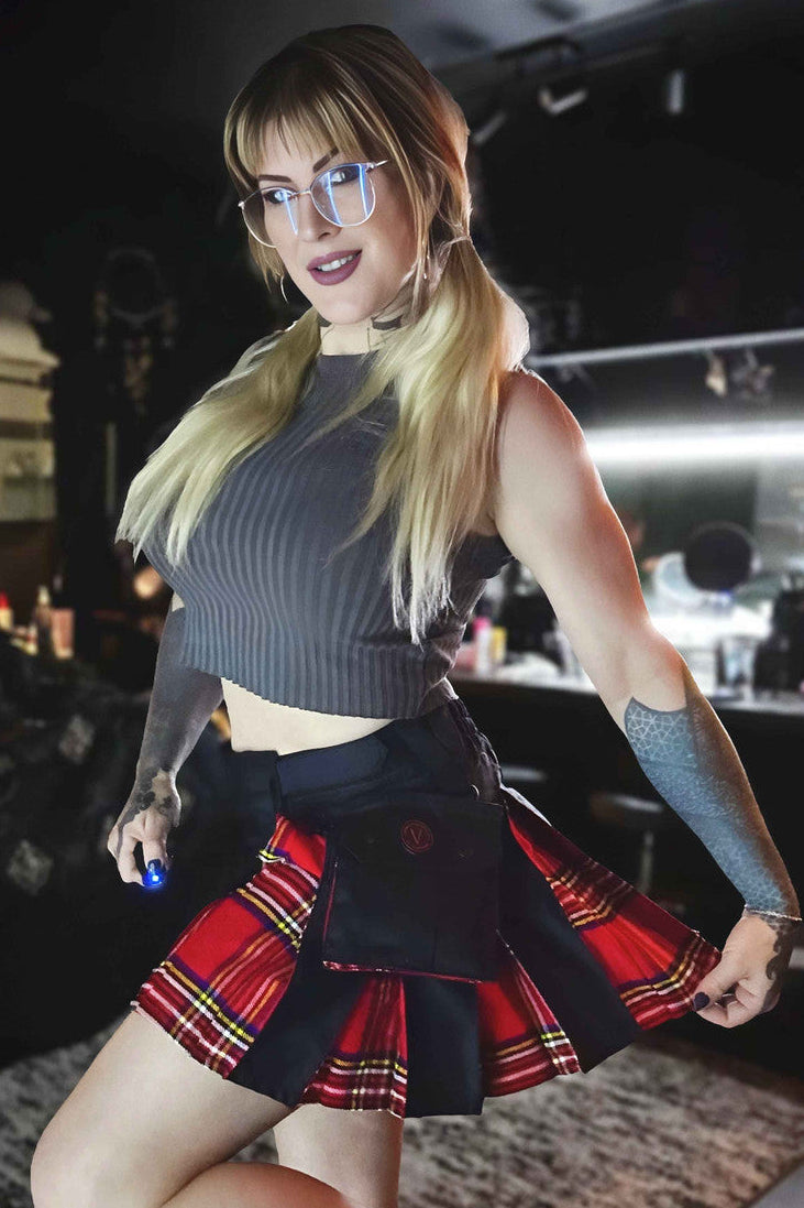 Woman in a black crop top and black and red plaid mini kilt posing in a bar setting.