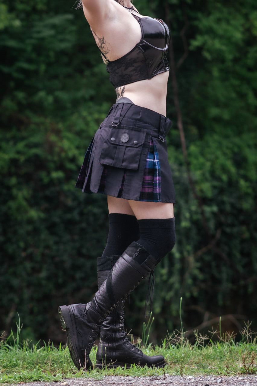 Right side view of a woman in a black mini kilt with blue and purple plaid details, also wearing a black top and leather boots