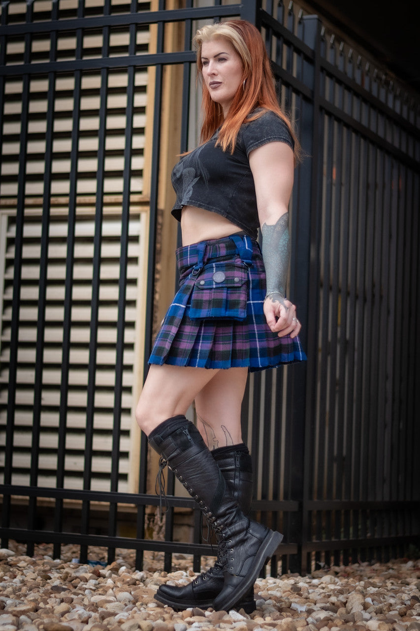 Full body side view of a woman wearing a blue and purple plaid mini kilt with a side pocket.