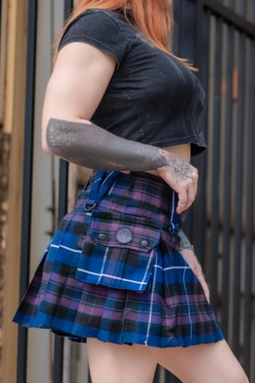 Person wearing a black t-shirt and blue and purple plaid mini kilt with tattoos on arms.