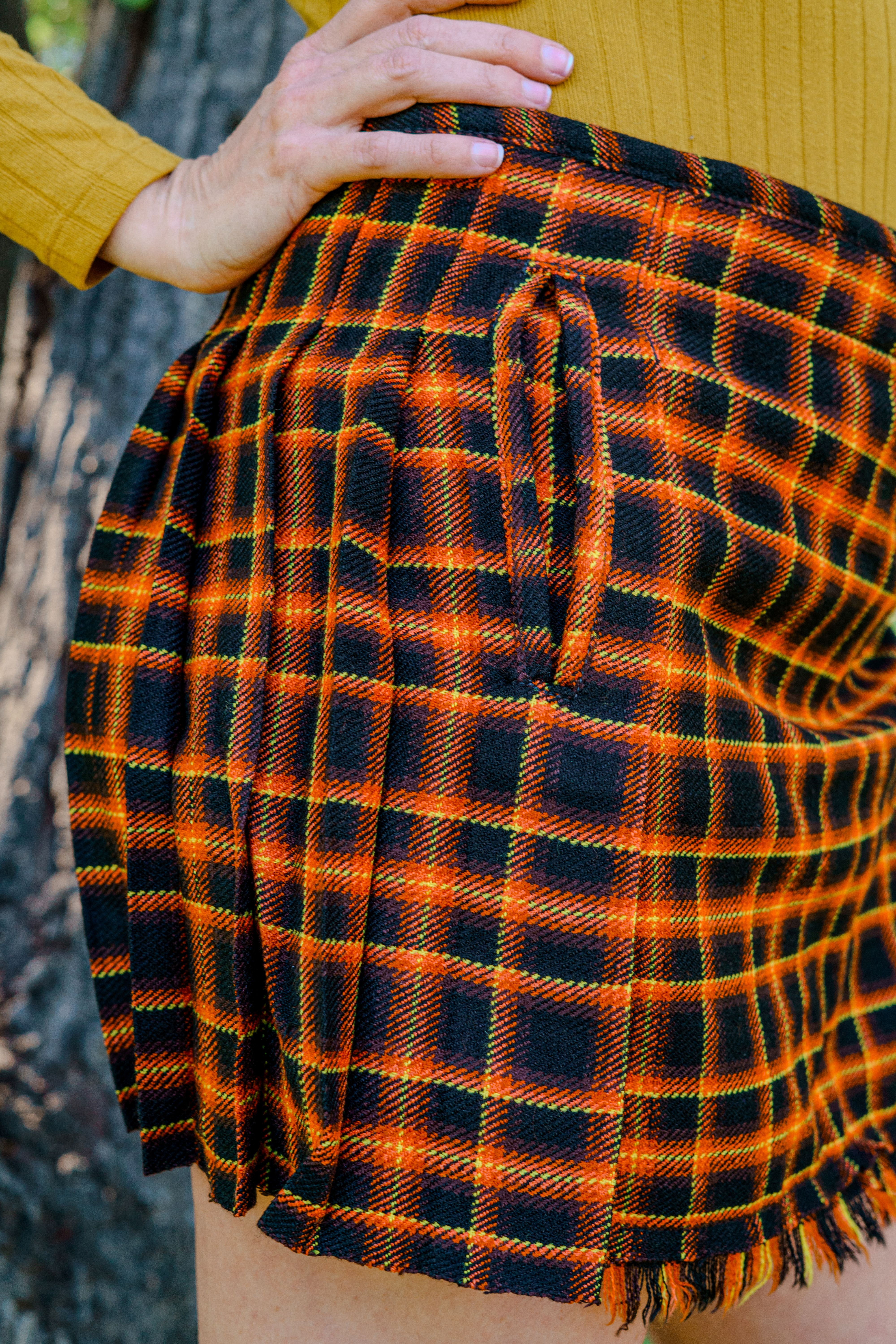 Orange and black plaid mini kilt worn by a person in a nature setting