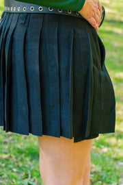 Close-up of a person wearing a pleated black mini kilt with a blurred green background