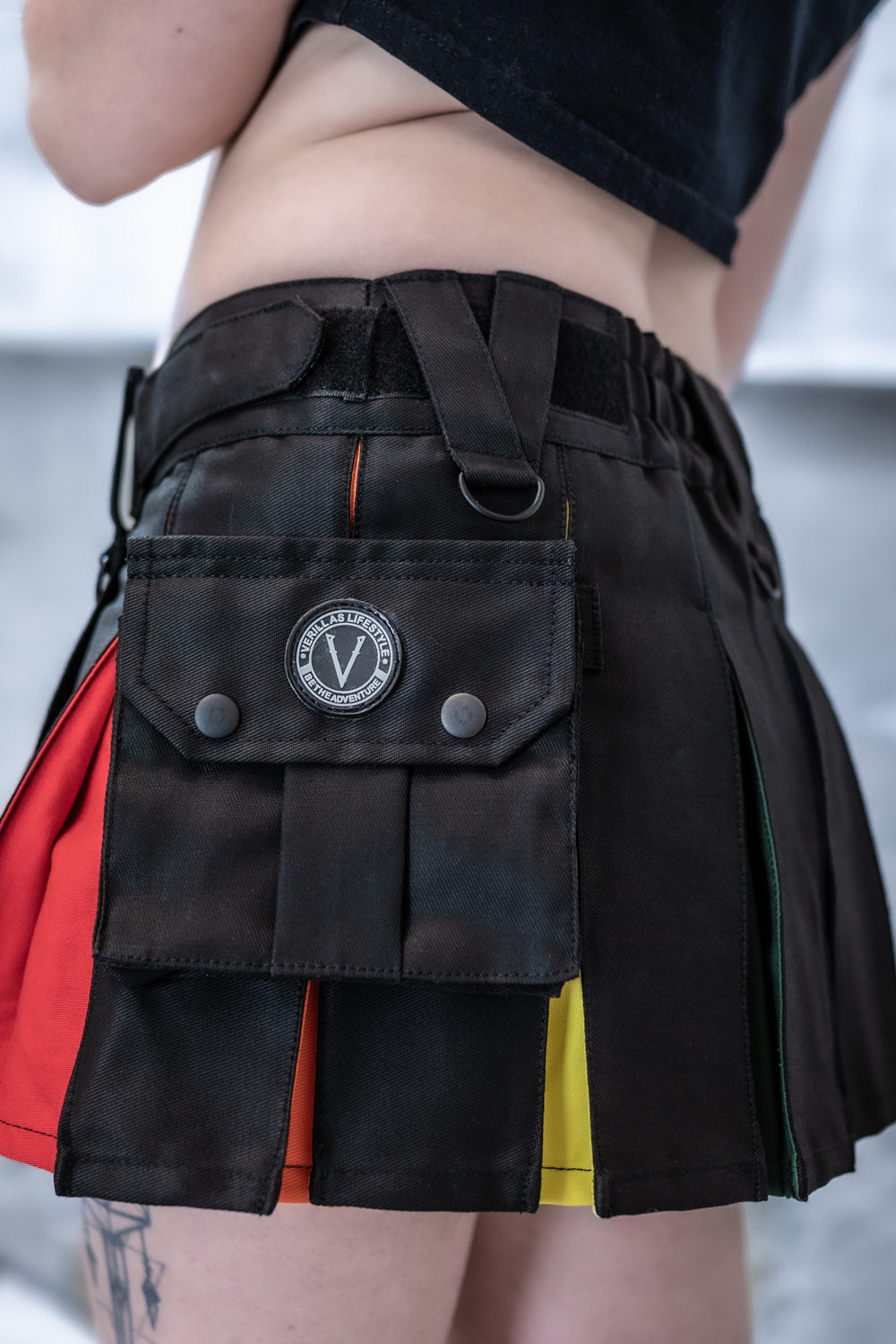 Very short black canvas kilt with rainbow pleats with a brand logo on a neutral background