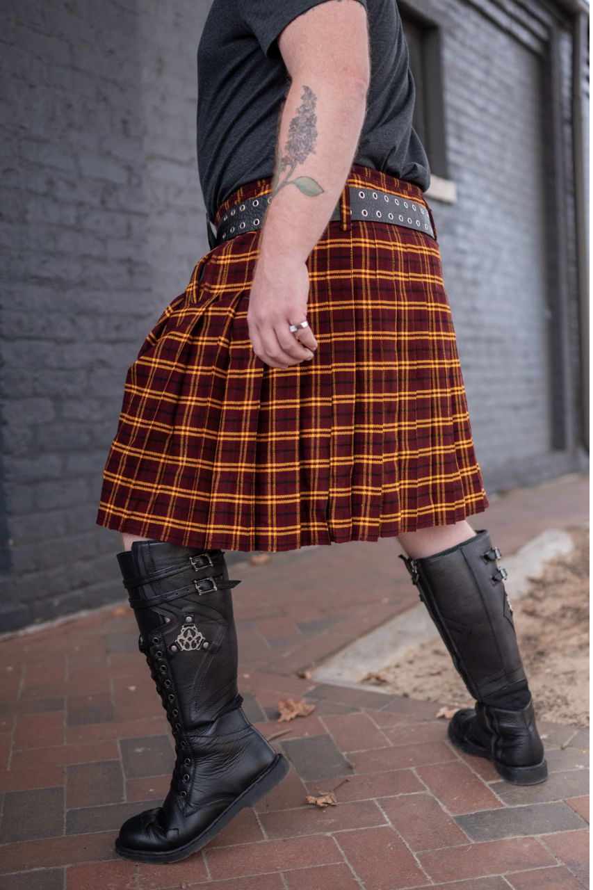 Person wearing a plaid kilt and black boots on a brick pavement.