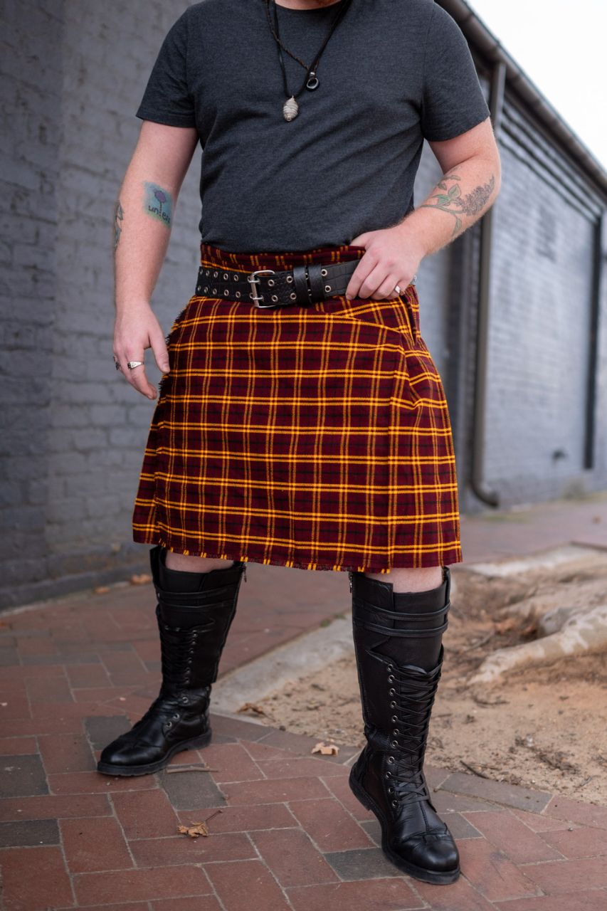Person wearing a red and yellow plaid kilt with black boots on a brick pavement.
