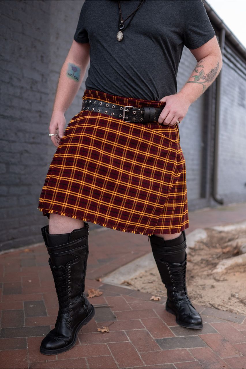 Person wearing a red and yellow plaid kilt with black boots on a brick pavement.