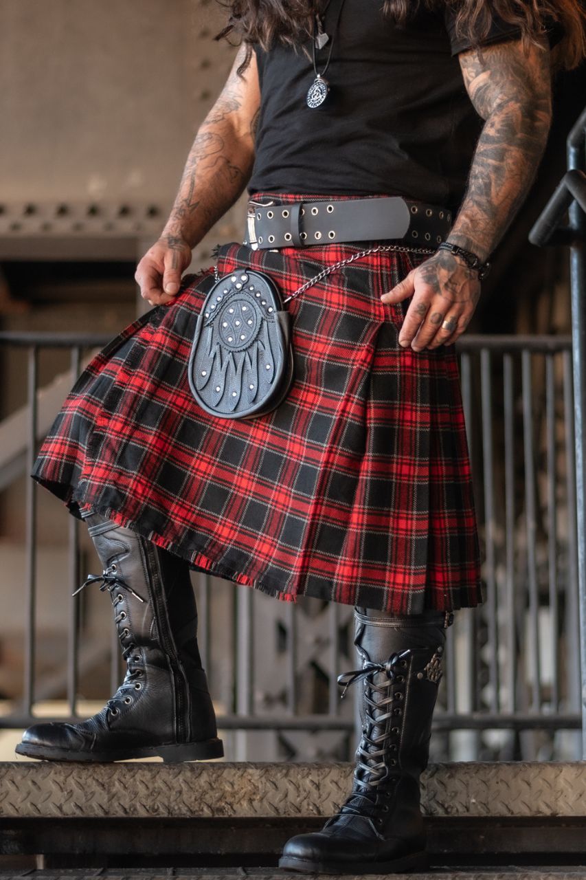 Person wearing a red and black plaid kilt with black boots indoors.