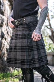 Person wearing a gray plaid kilt with black boots and gloves, standing against a natural background.