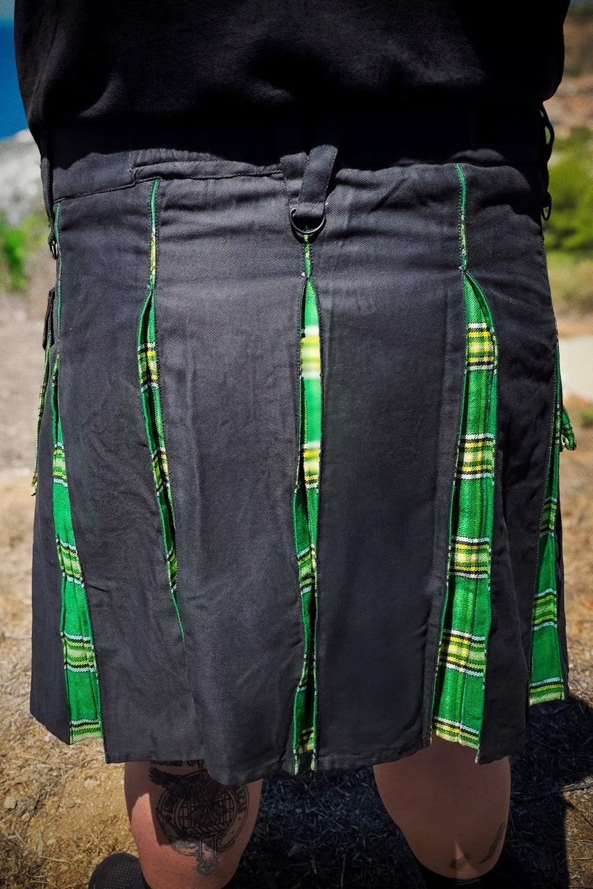 Person wearing a black kilt with green plaid accents on a natural background