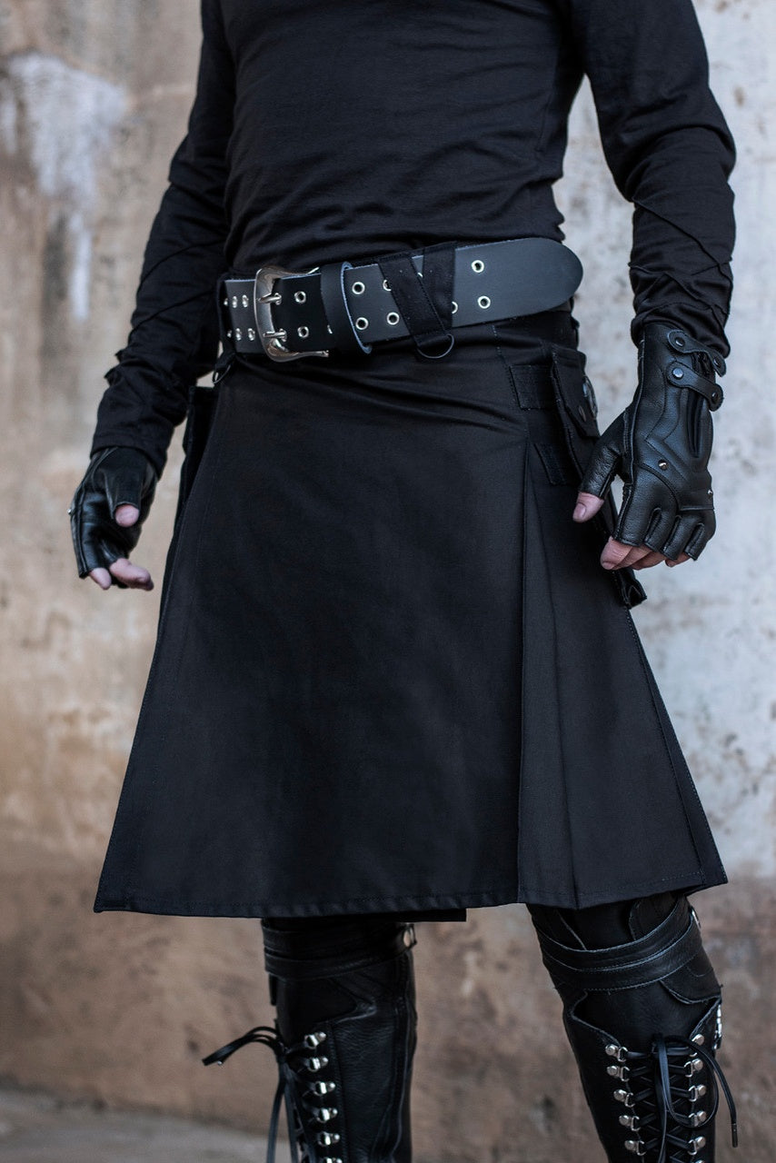 Person wearing a black kilt with black gloves and boots against a neutral background