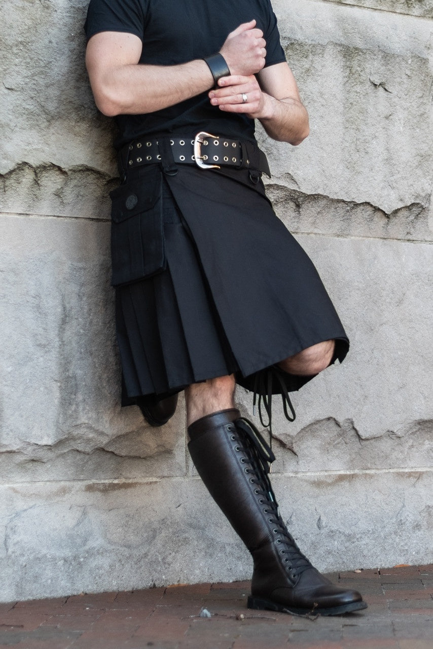 Person wearing a black kilt and boots against a stone wall.