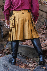 Person wearing a mustard yellow pleated kilt with a purple shirt and black boots outdoors.