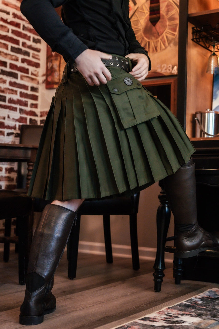 Person wearing a green pleated kilt and brown knee-high boots in an indoor setting.