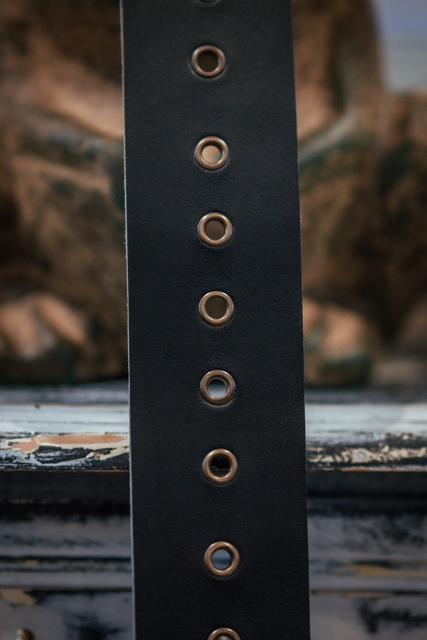 Close-up of a dark brown leather belt with brass eyelets on a blurred background