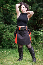 Person wearing a black kilt with orange accents outdoors