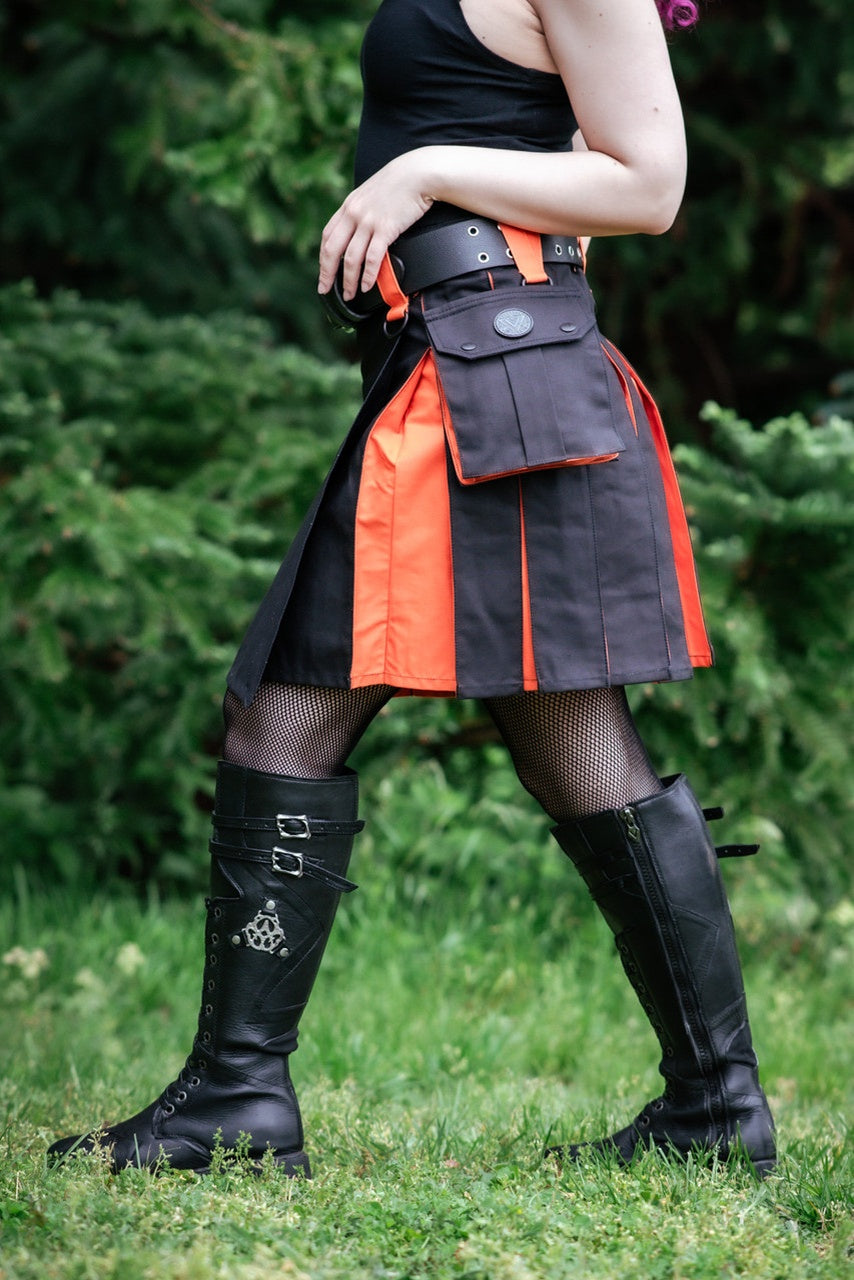 Person wearing a black and orange kilt with a bag, standing outdoors.