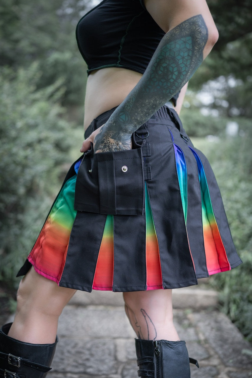Side view of a person wearing a black kilt with ombre rainbow panels in an outdoor setting.