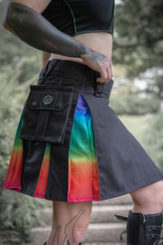 Person wearing a knee-length black kilt with ombre rainbow accents and tattoos visible.
