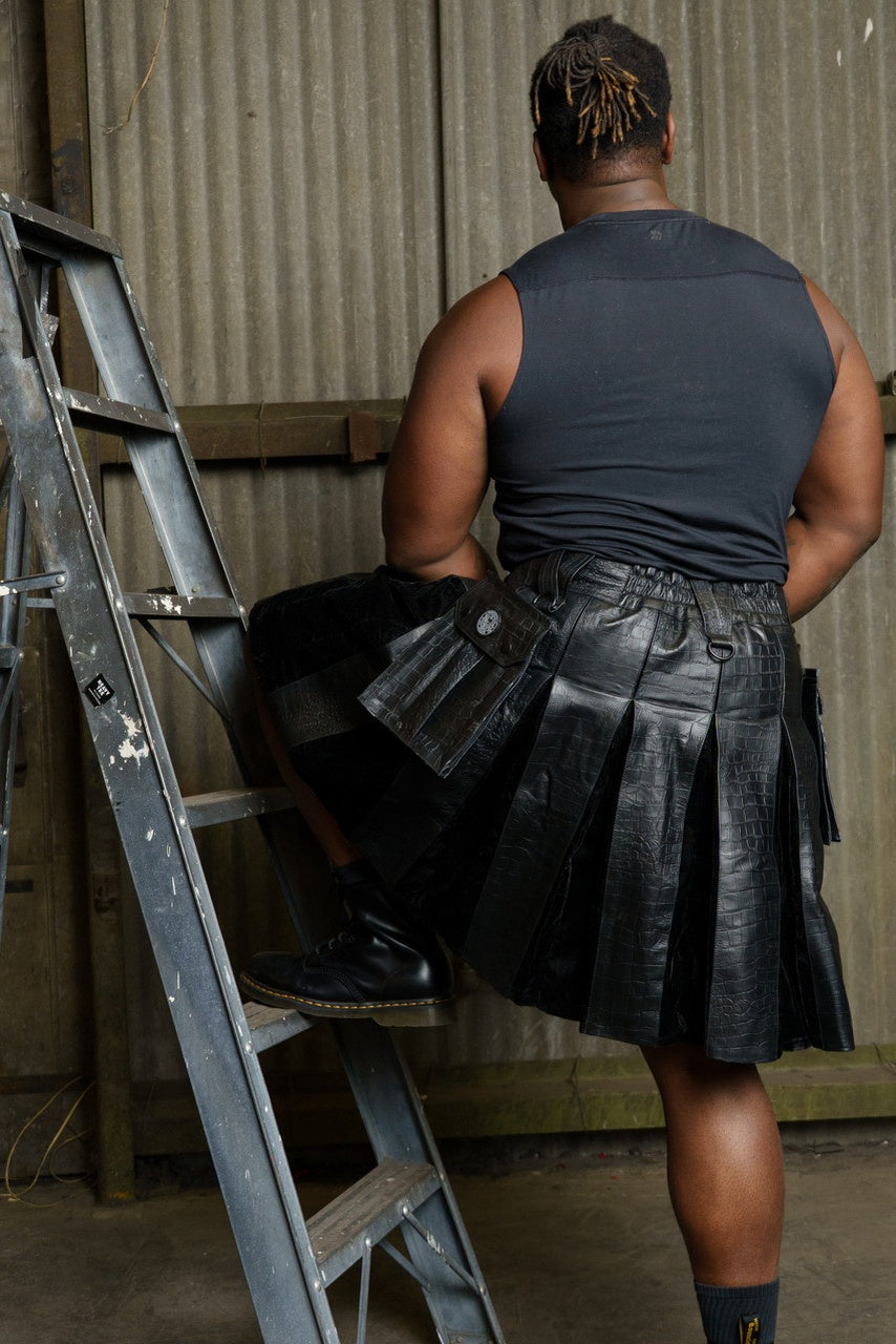 Back view of a person wearing a black scaled leather kilt standing next to a ladder in an industrial setting.