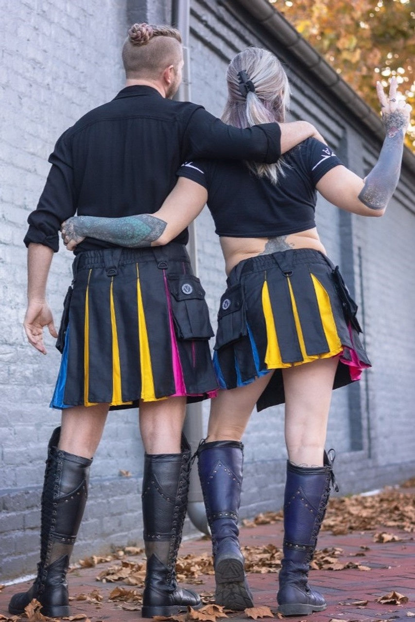 Two people wearing pan pride kilts and boots standing against a brick wall.