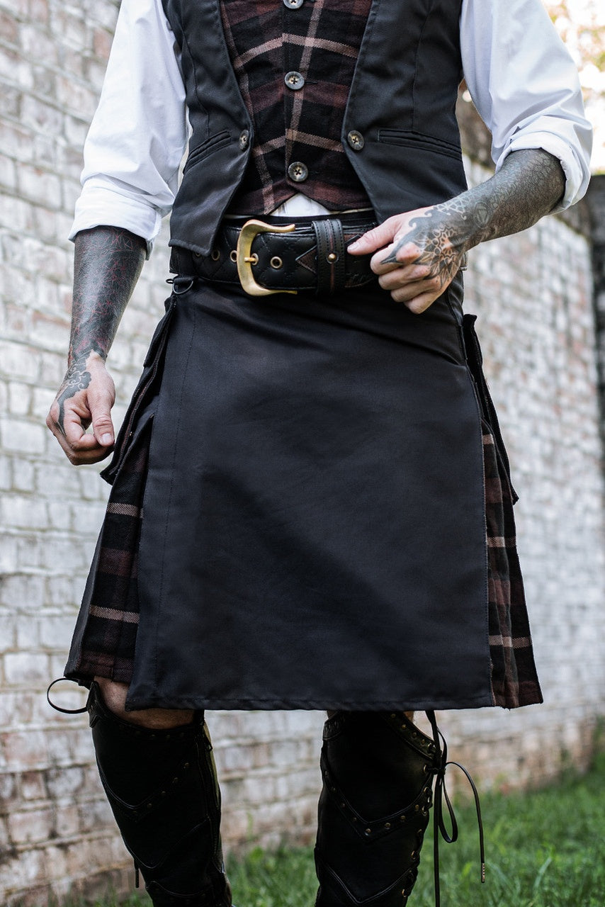Person wearing a black kilt with plaid accents, standing against a brick wall.