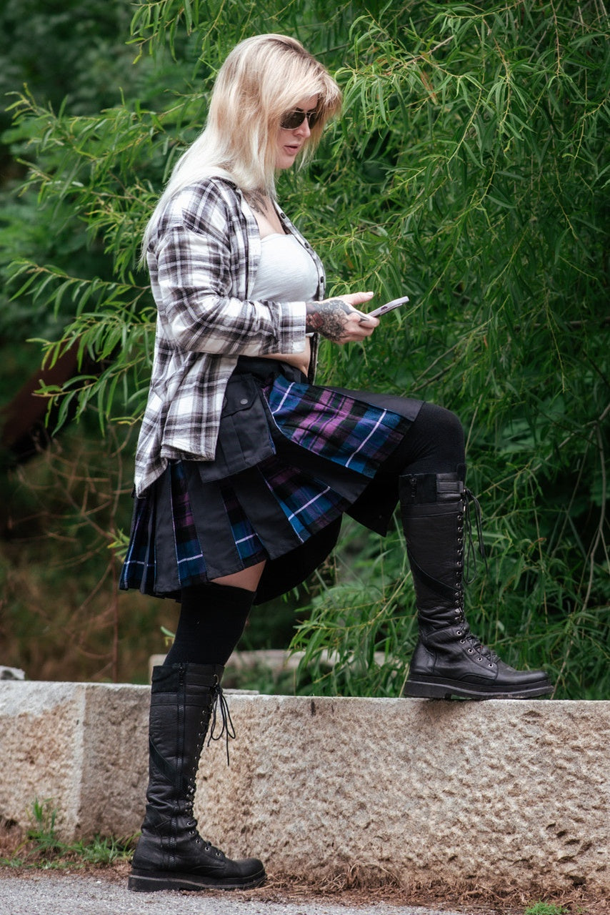 Person wearing a plaid shirt, skirt, and knee-high boots standing outdoors.