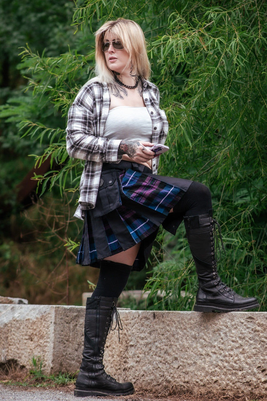 Person wearing a plaid skirt and black knee-high boots against a green foliage background