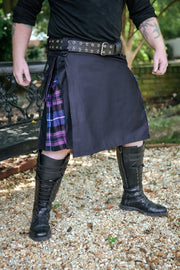 Person wearing a black kilt with a plaid pattern, black boots, and a belt outdoors.