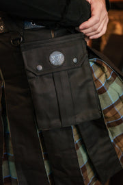 Close-up of dark pants with a pocket featuring a circular emblem, worn over a plaid garment.