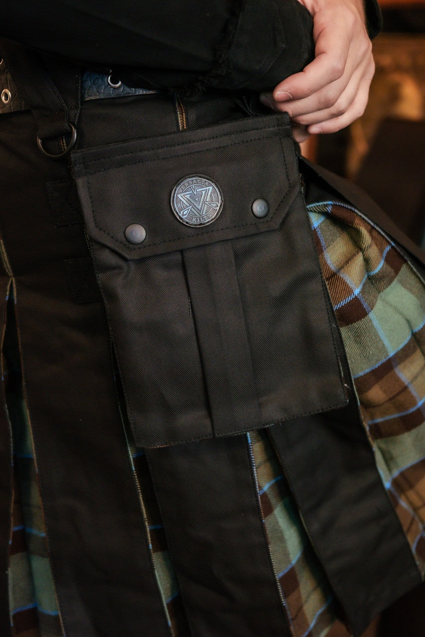 Close-up of dark pants with a pocket featuring a circular emblem, worn over a plaid garment.