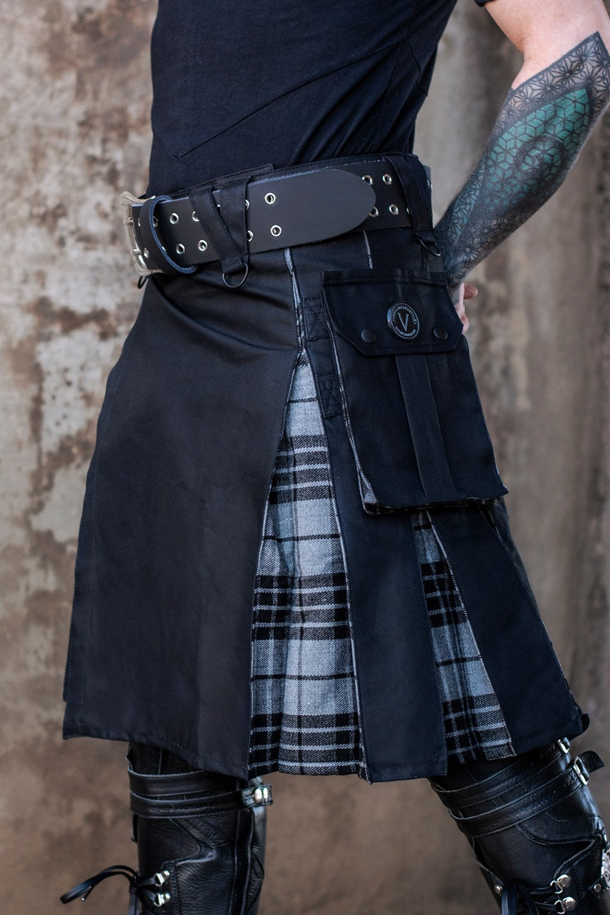 Person wearing a black kilt with plaid accents against a textured wall.