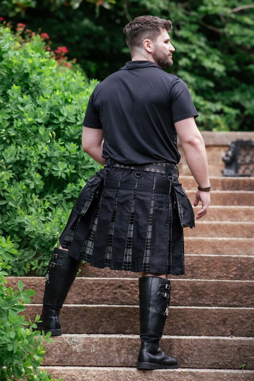Man wearing a black kilt standing on stone steps with greenery in the background