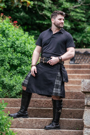 Man wearing a black kilt with plaid accents on stone steps outdoors.