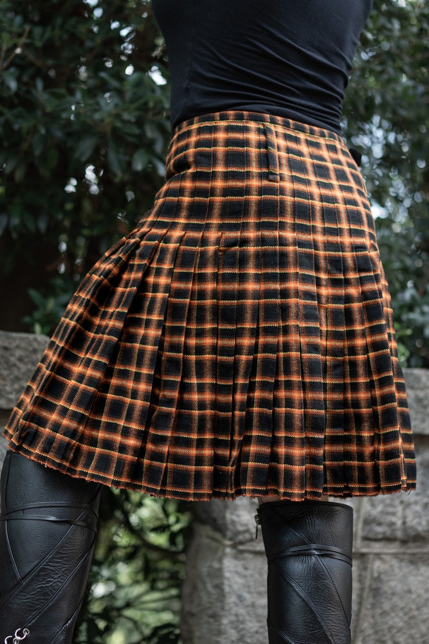 Back view of a person wearing an orange and black plaid kilt with a blurred natural background