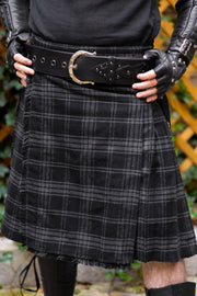 Person wearing a black plaid kilt with a belt and gloves outdoors.