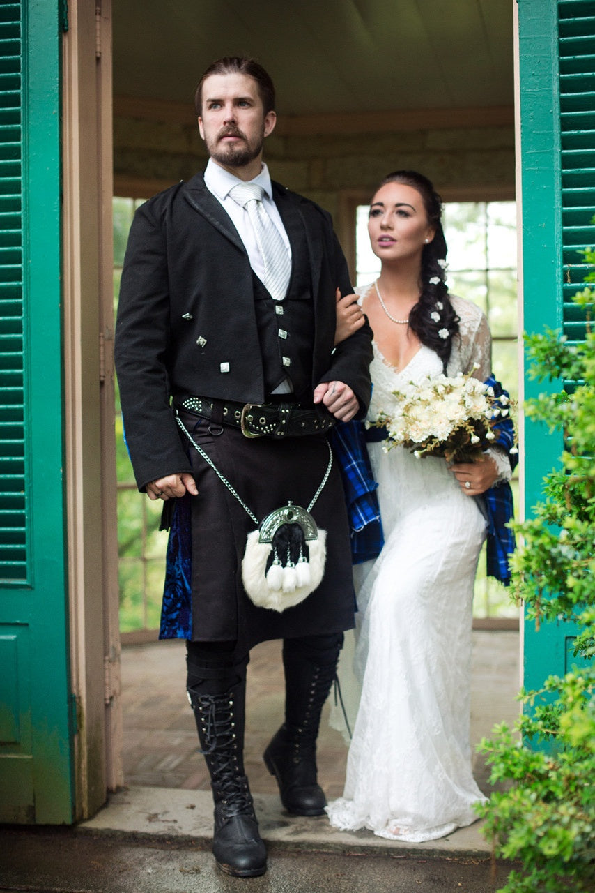 Man in traditional Scottish attire and woman in wedding dress standing together outdoors.