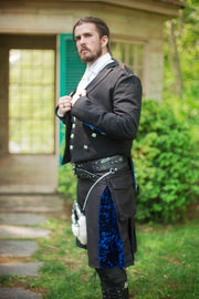 Man in a formal outfit with a black and blue velvet kilt standing outdoors.