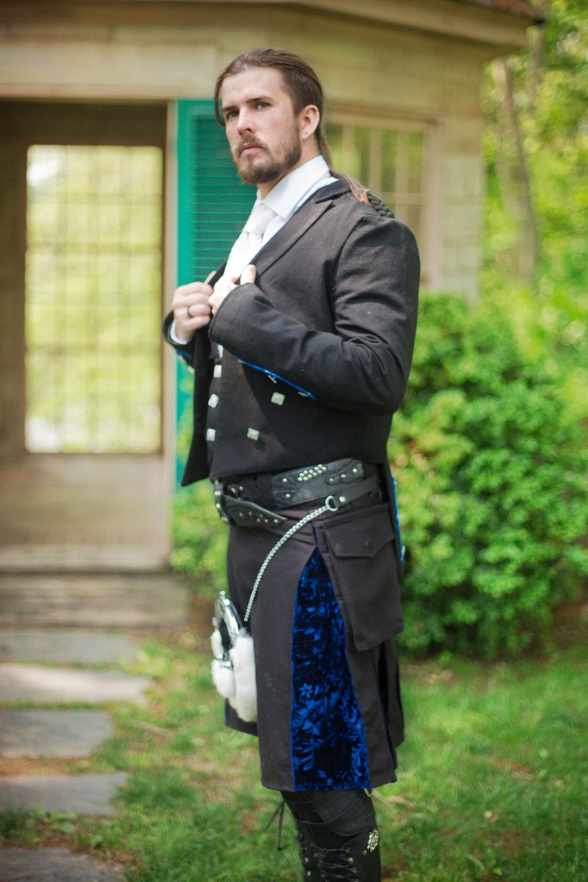 Man in a formal outfit with a black and blue velvet kilt standing outdoors.