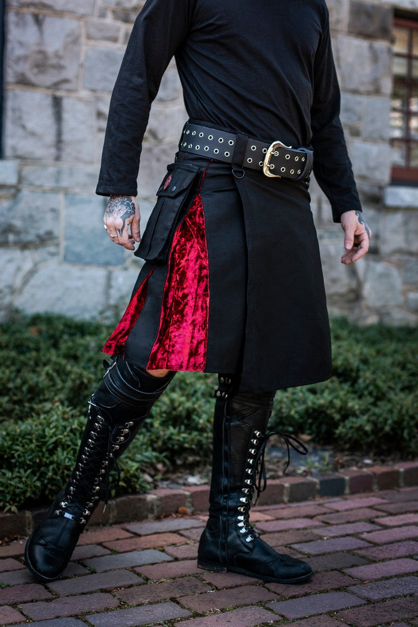Person wearing a black outfit with a red skirt and black boots in an outdoor setting.